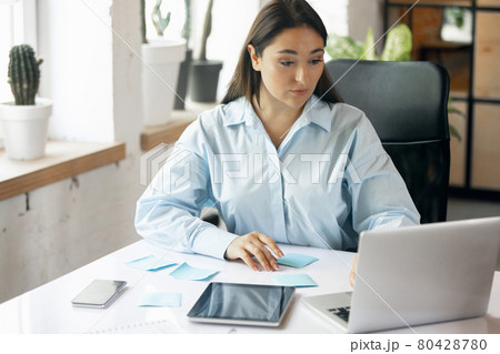 Young Caucasian woman, business lady during working office day. Using laptop, modern gadgets. Remote working. Workplace at office with PC, devices. Young Caucasian woman, business lady during working office day. Using laptop, modern gadgets. Remote working. Workplace at office with PC, devices. 80428780