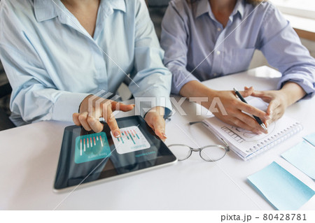 Two young women, colleguas during working day, business meeting. Using laptop, modern gadgets, notes. Workplace at office with PC, devices. 80428781