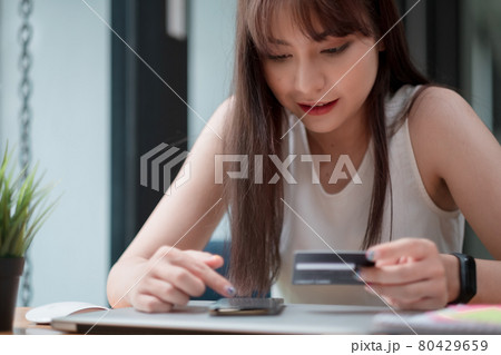 Portrait of young Asian woman smiling and holding a credit card and using a smartphone to shop online at home, online payment concept 80429659
