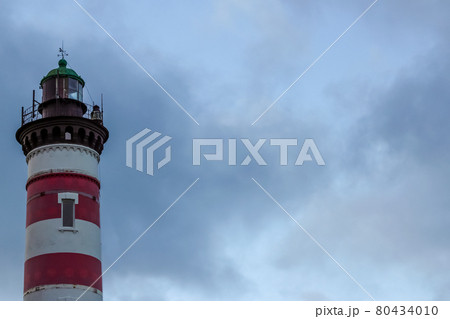 Red and white striped lighthouse on the background of a stormy sky. Free copy space for design or text 80434010