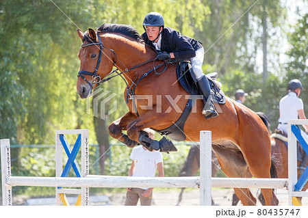 Young rider man jumping over the barrier 80435747