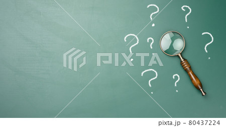 wooden magnifying glass and white chalk drawn question marks on a green chalk board. The concept of finding solutions, true or false 80437224