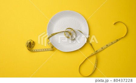 empty white ceramic plate and measuring tape on yellow background. Healthy nutrition concept 80437228