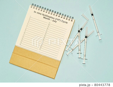 July IVF cycle calendar and disposable injection syringe on blue background 80443778
