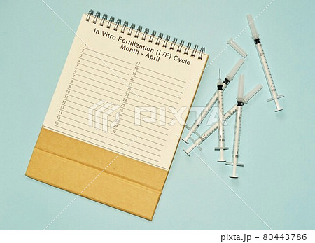 April IVF cycle calendar and disposable injection syringe on blue background 80443786