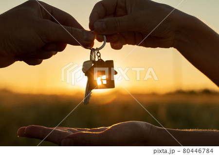 Close-up female gives a man the key to a new house on the background of a beautiful sunset. The concept of construction and real estate transactions. 80446784