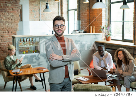 Young smiling businessman standing in front of working colleagues 80447797