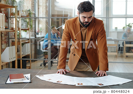 Serious hr manager bending over table while looking through resume 80448024