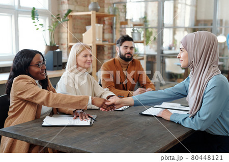 Happy African businesswoman shaking hand of Muslim female applicant 80448121