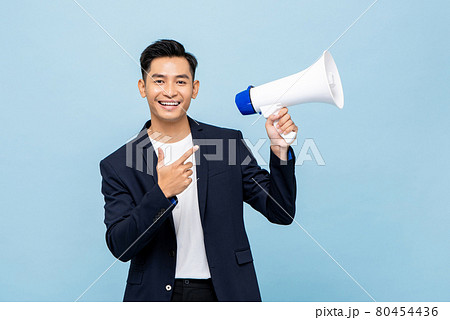 Smiling handsome Asian man holding megaphone in light blue isolated background 80454436