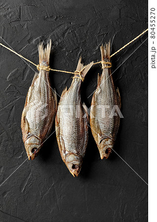 Dried salted roach fish hanging on rope on black wall 80455270