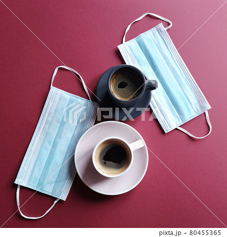 Surgical ear mask and a cup of coffee on a burgundy background. Medical mask protects against the virus of the crown or quarantine COVID-19. Biological concept of life. Lifestyle and Flatlay. 80455365