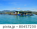 a floating fishing village in a sea bay, against a backdrop of mountains covered with tropical vegetation, clouds and a blue sky 80457230