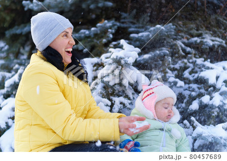family portrait in the winter forest, mother and baby sitting and playing with snow, beautiful nature with snowy fir trees 80457689