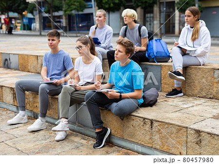 Teen students sitting with workbooks in schoolyard 80457980