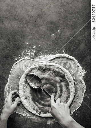 Making a pizza spreding tomato sauce on the dough 80460757