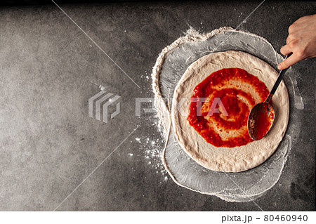 Making a pizza spreding tomato sauce on the dough 80460940