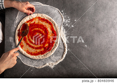 Making a pizza spreding tomato sauce on the dough Making a pizza spreding tomato sauce on the dough 80460946
