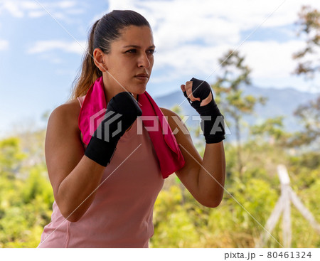 Strong Latina woman in boxing position with gloves and towel outdoors 80461324