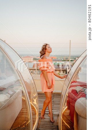 beautiful woman in a pink dress in a rooftop cafe at sunset beautiful woman in a pink dress in a rooftop cafe at sunset 80462191