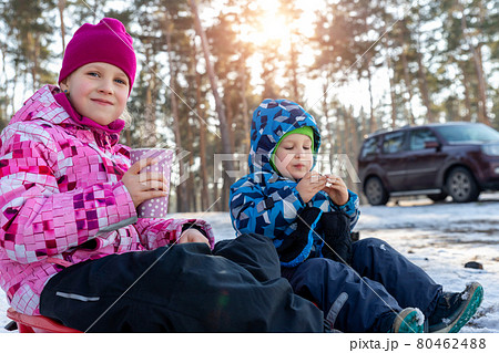 Two cute adorable beautiful caucasian little siblings children boy girl enjoy drinking warm drink tea or chocolate in paper cup and eat on bright sunny winter morning forest family picnic outside Two cute adorable beautiful caucasian little siblings children boy girl enjoy drinking warm drink tea or chocolate in paper cup and eat on bright sunny winter morning forest family picnic outside 80462488