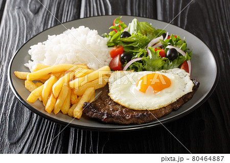 Bitoque is a beloved Portuguese dish that includes lean steak accompanied by rice and french fries topped with a fried egg closeup in the plate. Horizontal 80464887