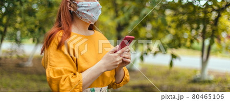 COVID-19 Coronavirus Young woman wearing medical mask uses smartphone app in city park during pandemic COVID-19 Coronavirus Young woman wearing medical mask uses smartphone app in city park during pandemic 80465106