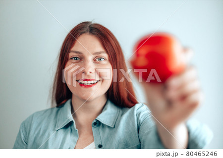 Portrait of a cheerful young woman eating red apple on gray wall background. Healthy nutrition diet. Apple vitamin snack. 80465246