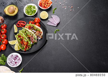 Mexican tacos with beef, tomatoes, avocado, onion and salsa sauce on a dark concrete background Mexican tacos with beef, tomatoes, avocado, onion and salsa sauce on a dark concrete background 80469350