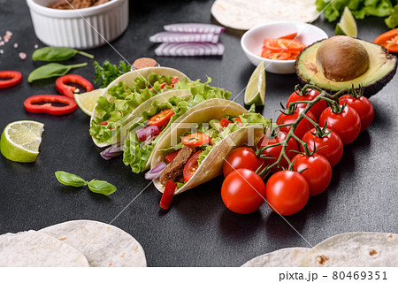 Mexican tacos with beef, tomatoes, avocado, onion and salsa sauce on a dark concrete background Mexican tacos with beef, tomatoes, avocado, onion and salsa sauce on a dark concrete background 80469351