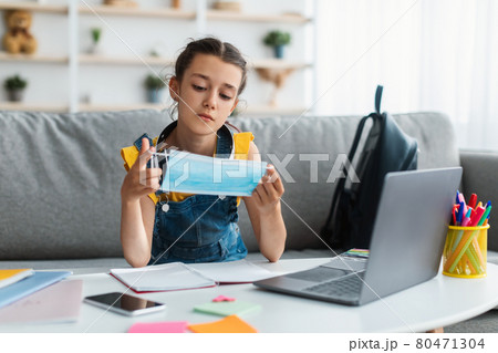 Sad girl holding surgical mask studying at home with laptop 80471304