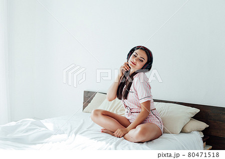 portrait of a beautiful brunette woman listening to music in headphones in the bedroom on the bed portrait of a beautiful brunette woman listening to music in headphones in the bedroom on the bed 80471518