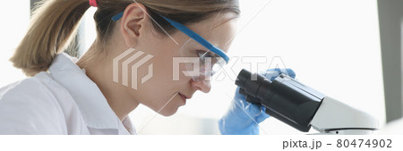 Woman scientist with glasses conducts research through microscope Woman scientist with glasses conducts research through microscope 80474902