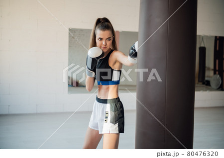 Beautiful kickboxing woman training punching bag in fitness studio. 80476320