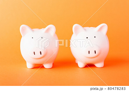 Front two small white fat piggy bank, studio shot isolated on orange Front two small white fat piggy bank, studio shot isolated on orange 80478283