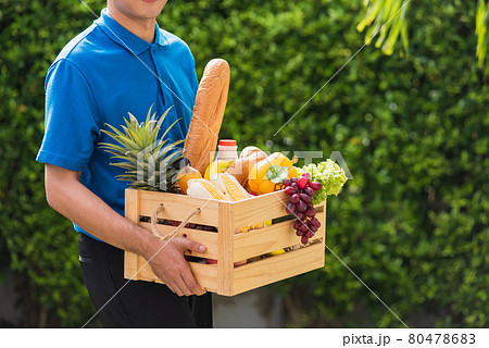 Man farmer wears delivery uniform he holding full fresh vegetables and fruits in crate wood box Man farmer wears delivery uniform he holding full fresh vegetables and fruits in crate wood box 80478683