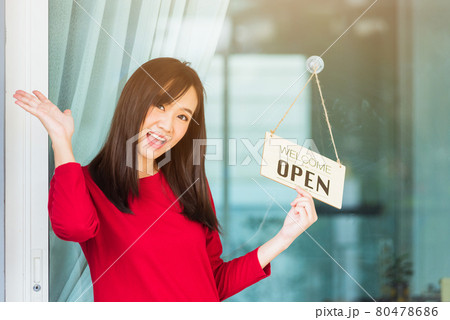 Woman glad smiling she notice sign wood board label "WELCOME OPEN" hanging through glass door front shop Woman glad smiling she notice sign wood board label "WELCOME OPEN" hanging through glass door front shop 80478686