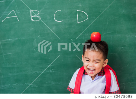 Child boy from kindergarten in student uniform with school bag and red apple on head smiling Child boy from kindergarten in student uniform with school bag and red apple on head smiling 80478698
