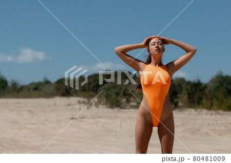 Young woman in orange swimsuit standing on sand 80481009