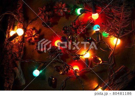 Christmas pine cones, lights and parts of tree bark. Colorful vintage stones. Bronze surface background. Selective lighting scene. Top view photo. 80481186