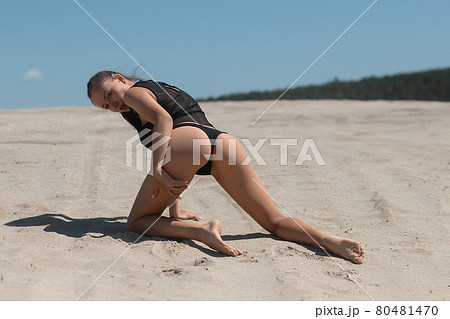 Slim woman in black underwear kneeling on sand 80481470