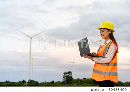female engineer working with laptop computer against wind turbine farm female engineer working with laptop computer against wind turbine farm 80483460