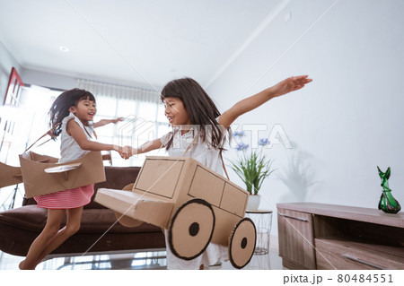 girl playing with cardboard toy airplane at home 80484551