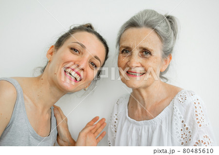 Happy senior mother is hugging her adult daughter, the women are laughing together, sincere family of different age generations having fun on white background, mothers day. 80485610
