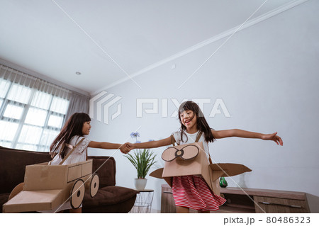 girl playing with cardboard toy airplane at home 80486323