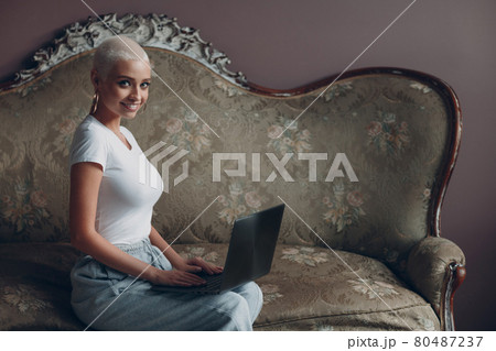 Millenial young woman with short blonde hair portrait sitting with laptop on vintage sofa. 80487237