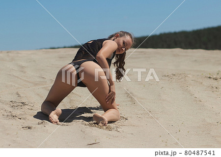 Slim woman in black underwear kneeling on sand 80487541