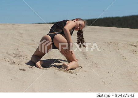 Slim woman in black underwear kneeling on sand 80487542