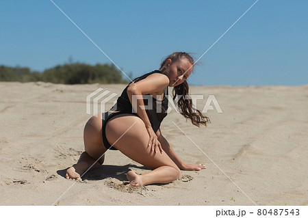 Slim woman in black underwear kneeling on sand 80487543