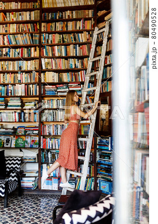 Happy student girl or woman with picking up books in library. Young woman casual daily lifestyle standing with books on wooden stairs joyful. Happy student girl or woman with picking up books in library. Young woman casual daily lifestyle standing with books on wooden stairs joyful. 80490528